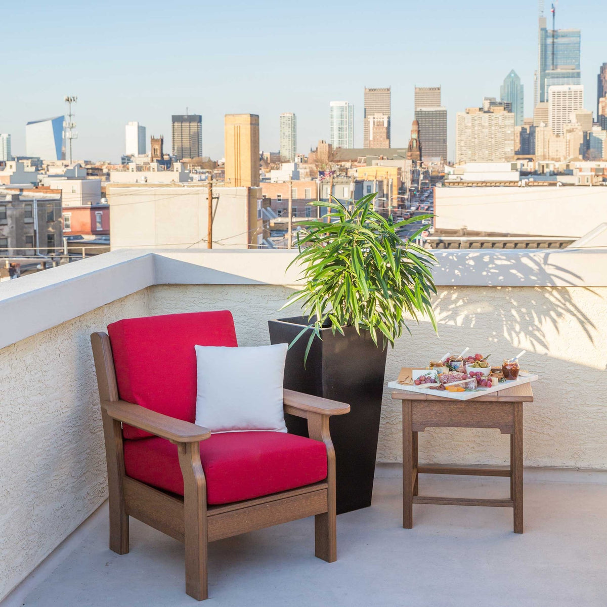 Mahogany poly patio chair with red replacement cushions and a white pillow on a rooftop deck with a city skyline