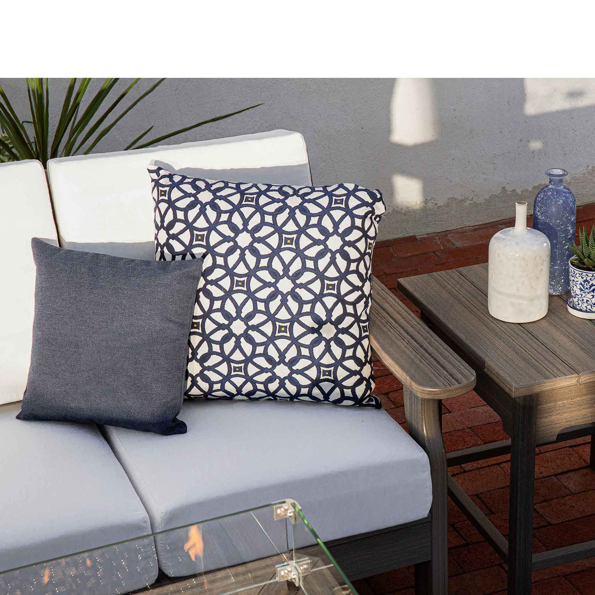White cushioned poly sofa with navy medallion and gray pillows beside a gray side table on a brick patio