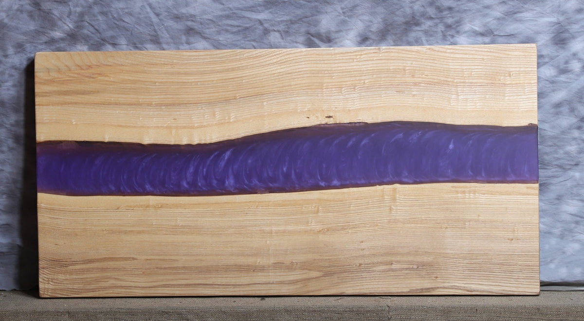 Ash live edge slab with straight blond grain divided by a wide purple epoxy river down the middle