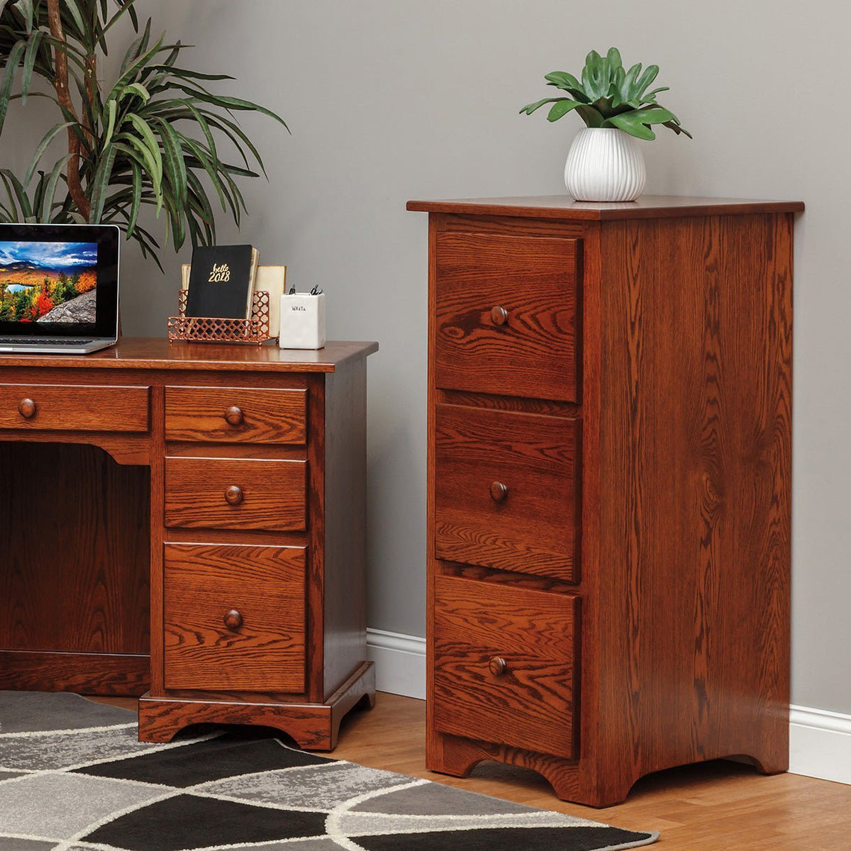Three-drawer solid oak file cabinet in a warm cherry stain standing beside a matching oak desk in a home office