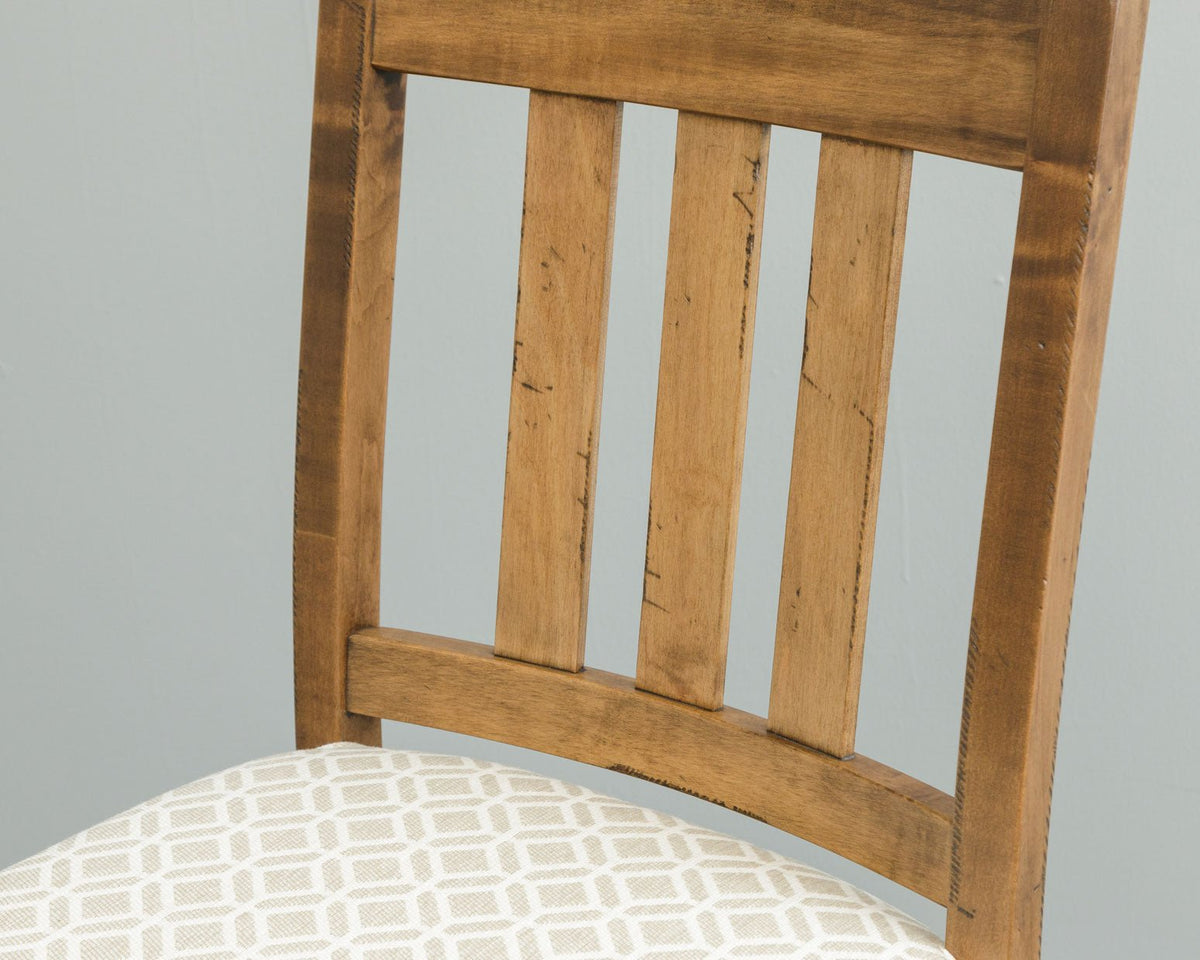 Close view of the distressed maple bar chair back showing three vertical slats above a patterned seat cushion