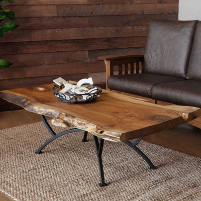 Live edge walnut coffee table on a black arched iron base, styled with a scroll bowl beside a leather sofa