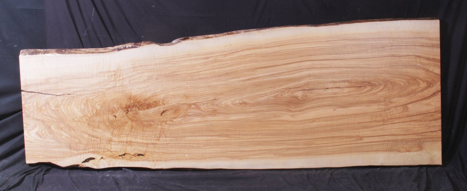 Long ash live edge slab with straight flowing grain, a few knots and undulating bark edges on a black backdrop