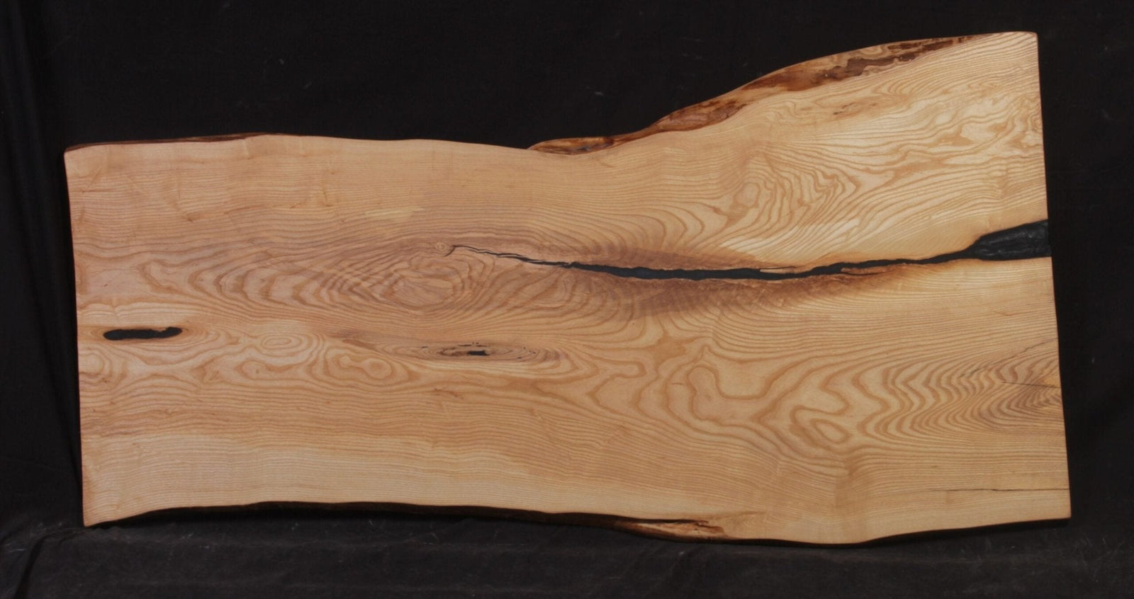 Ash live edge slab with a black epoxy filled crack running the length and swirling honey and cream grain