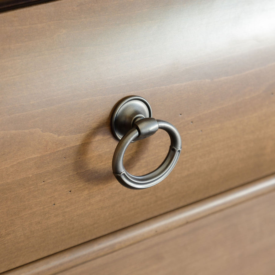 Close-up of an antique pewter ring pull mounted on the smooth light stained drawer front of a bedside chest