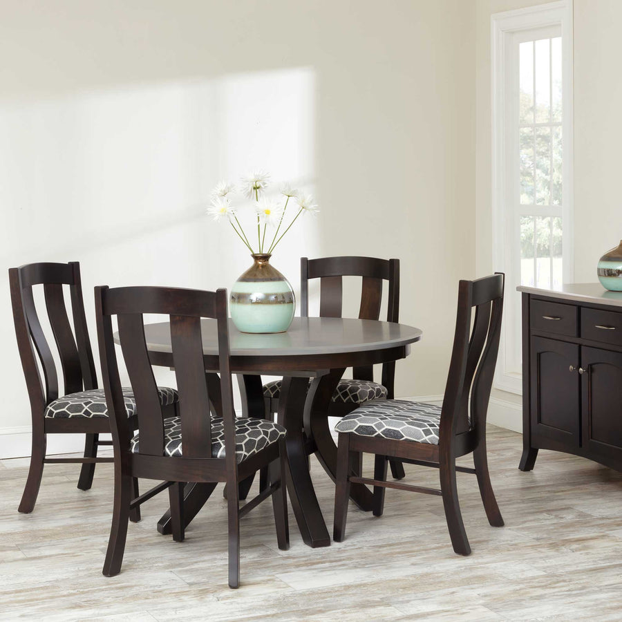 Espresso round pedestal dining table with four slat back chairs upholstered in gray print fabric beside a matching sideboard