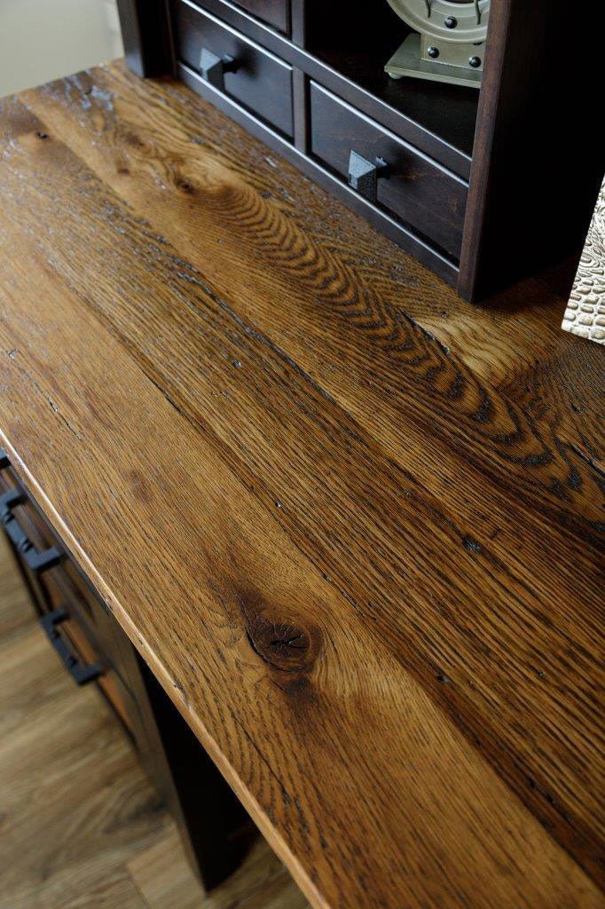 Reclaimed oak desk top with knots, saw marks and nail holes, with the dark hutch drawers behind it