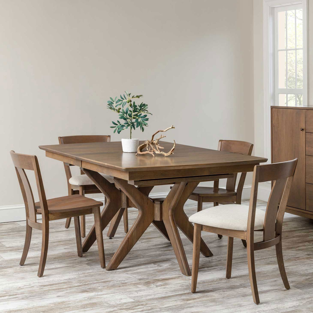 Mid century style dining table with crossed pedestal legs and four chairs with cream upholstered seats
