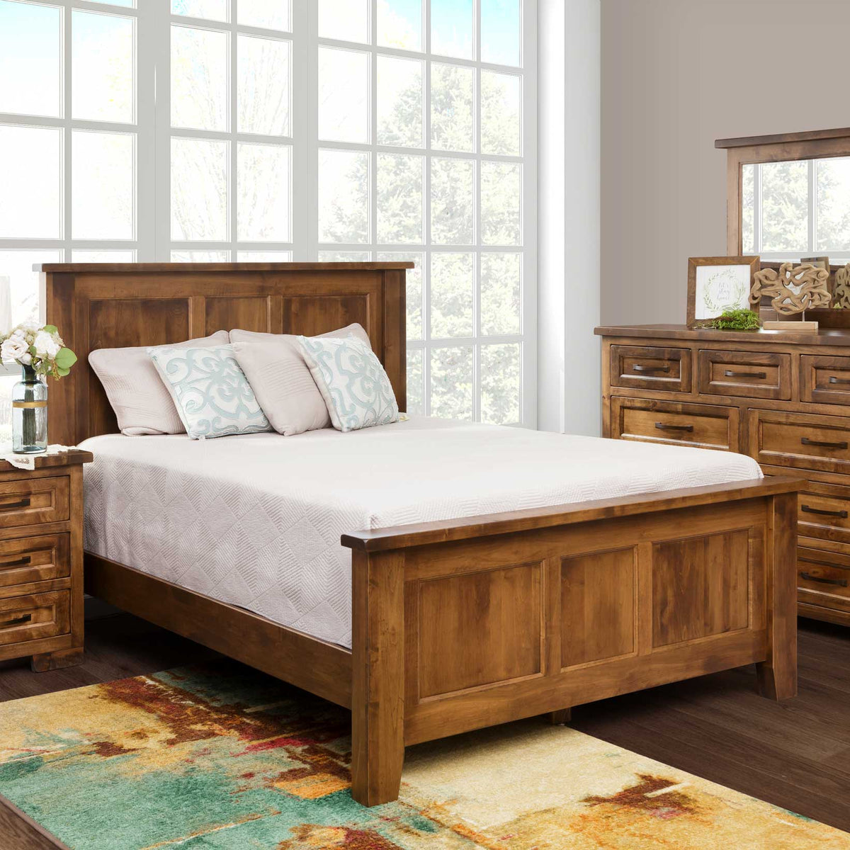 Solid brown maple panel bed in a warm rustic finish shown in a bedroom set with matching nightstand, dresser and mirror by bright windows