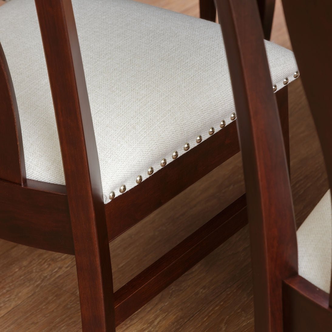 Close-up of a dining chair's cream linen seat with brass nailhead trim and curved cherry back slats