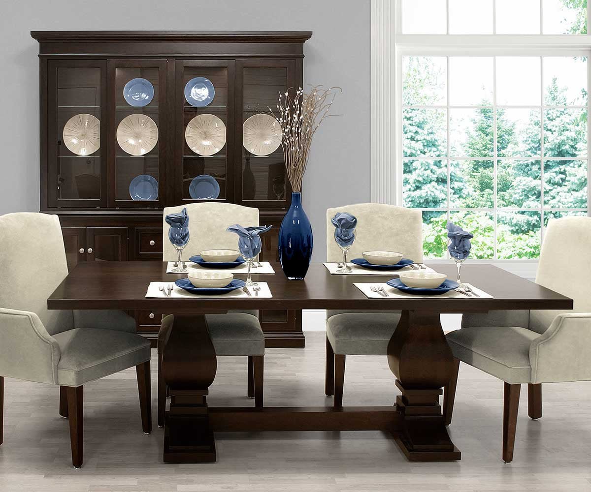 Dark espresso pedestal dining table set with cream upholstered chairs and a lighted china cabinet behind