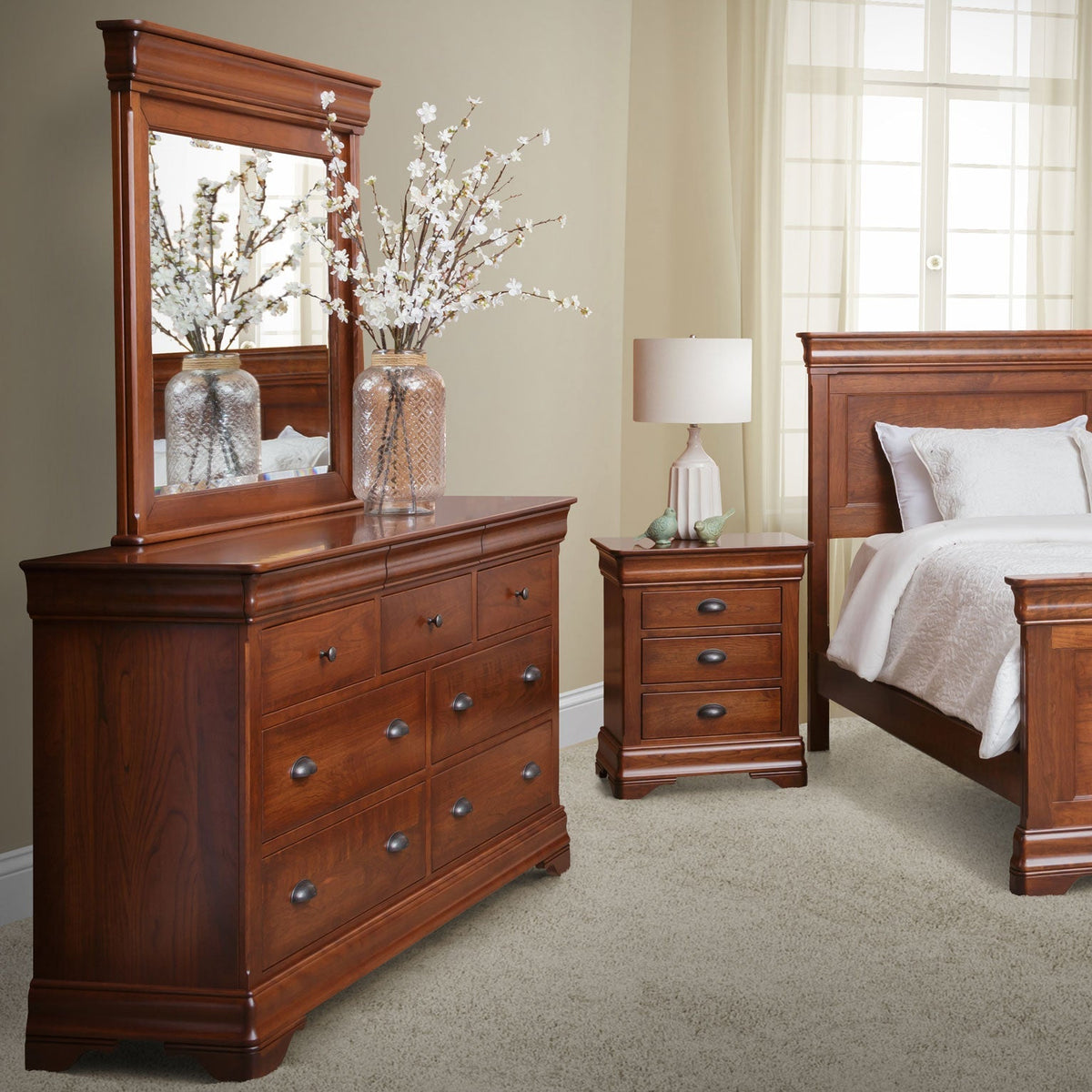 Cherry triple dresser with mirror and blossom branches beside a three-drawer nightstand and sleigh bed