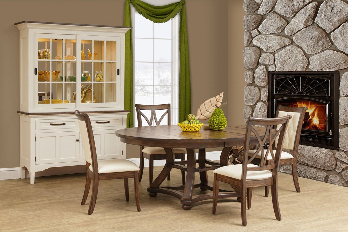 Dining room scene with a round rustic table, cream upholstered chairs, white china hutch and stone fireplace