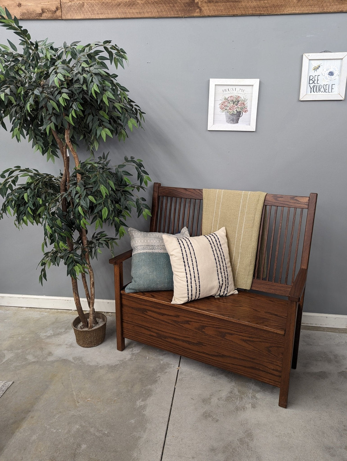 Dark stained Mission deacon bench with spindle back styled with striped throw pillows and a blanket by a gray wall