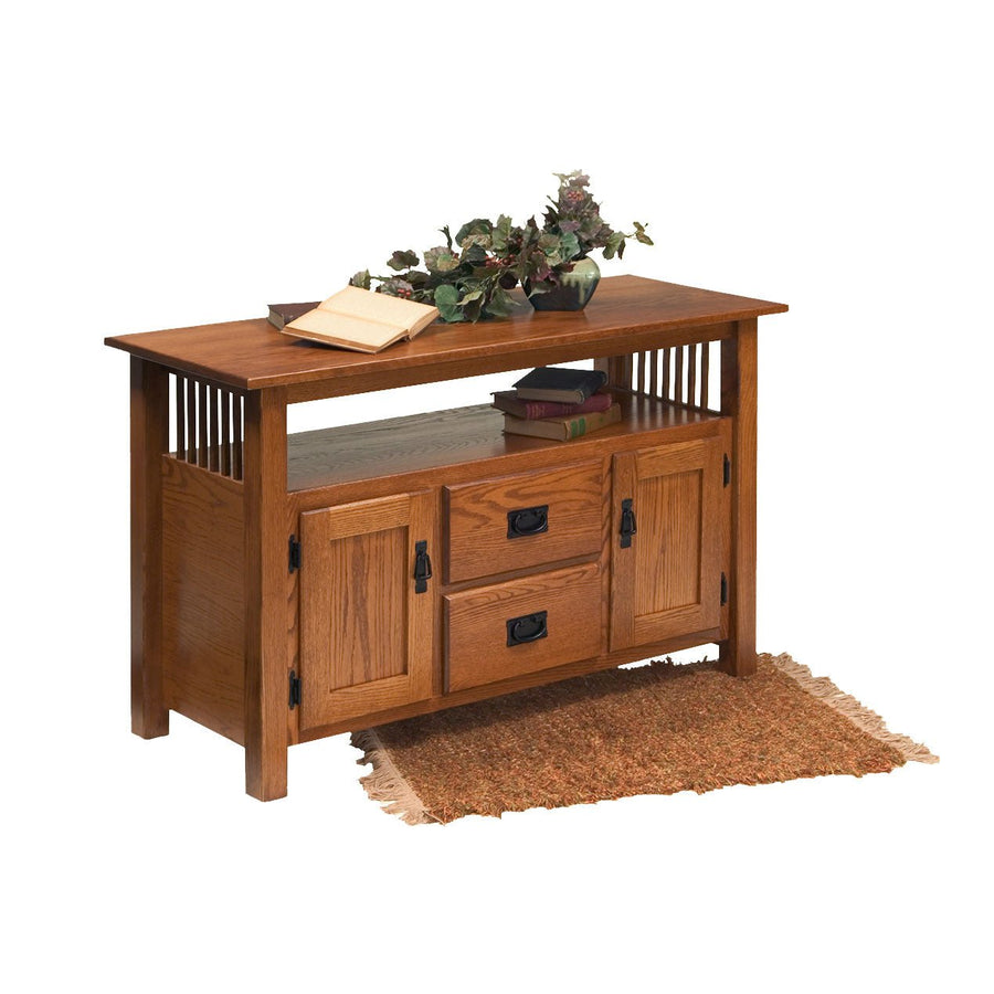 Mission oak tv console with two drawers, two paneled cabinet doors and an open shelf holding books and flowers