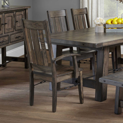 Weathered gray oak dining arm chairs with slat backs pulled up to a rustic trestle table and sideboard