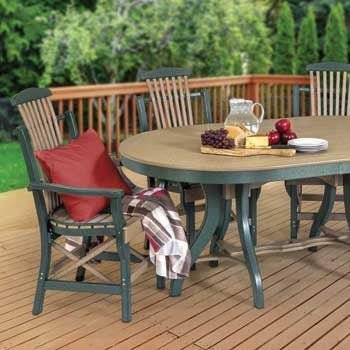 Green poly oval patio dining table with slat back arm chairs, set with fruit and cheese on a deck