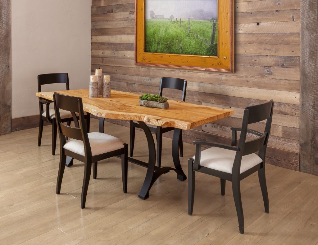 Live edge dining table with black metal legs and four black chairs with cream seats by a barnwood wall