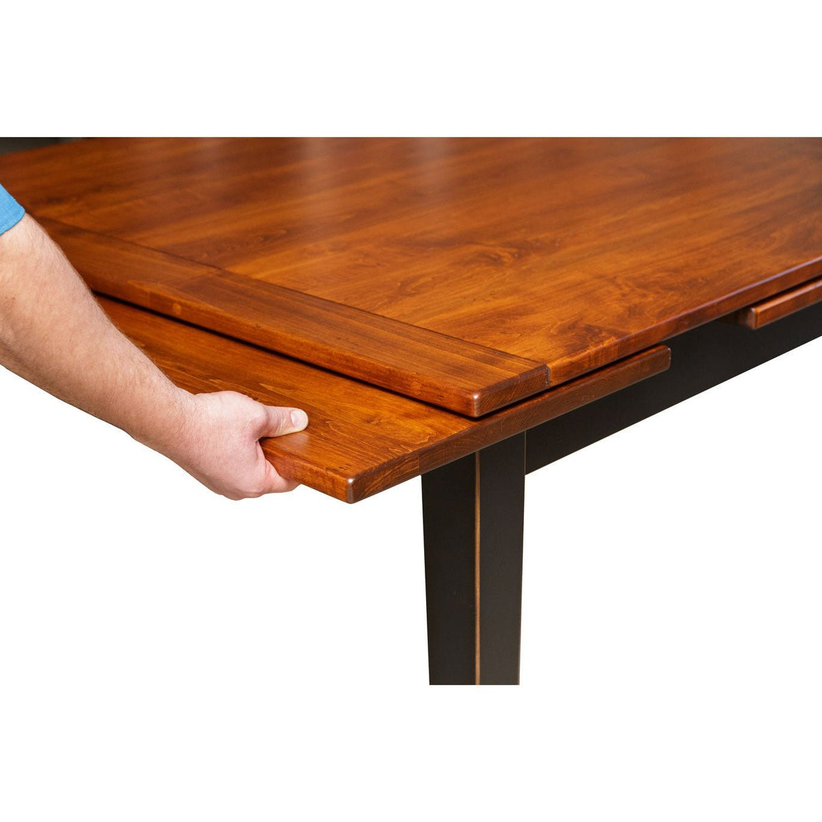 Hand pulling out the draw leaf extension on a cherry-topped dining table with a black painted base