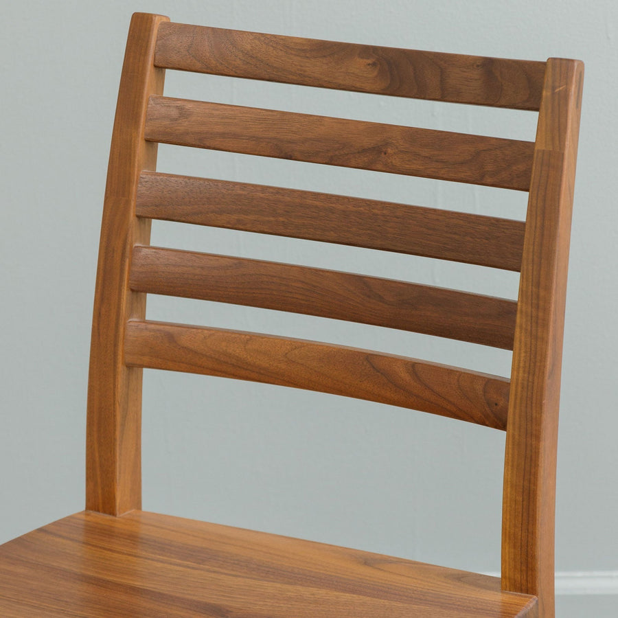 Close view of a walnut dining chair back with five gently curved horizontal slats above a solid seat