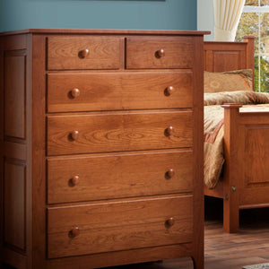 Cherry chest of six drawers photographed in a bedroom beside a panel bed with patterned bedding