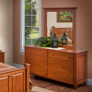 Cherry six drawer double dresser with mirror, greenery and lanterns beside a bright window