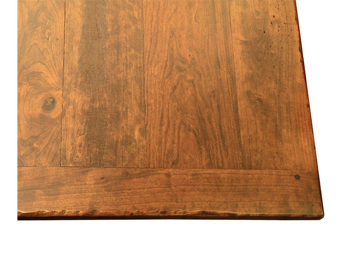 Corner detail of a rustic dining table top showing plank seams, wormholes and a soft wavy edge