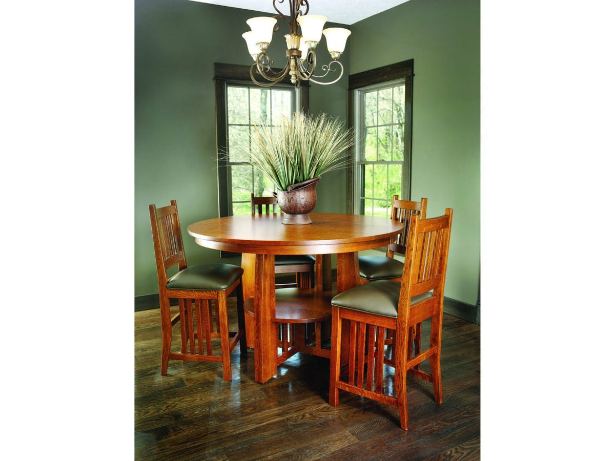 Round oak table with four slat back leather seat chairs in a dining room with green walls
