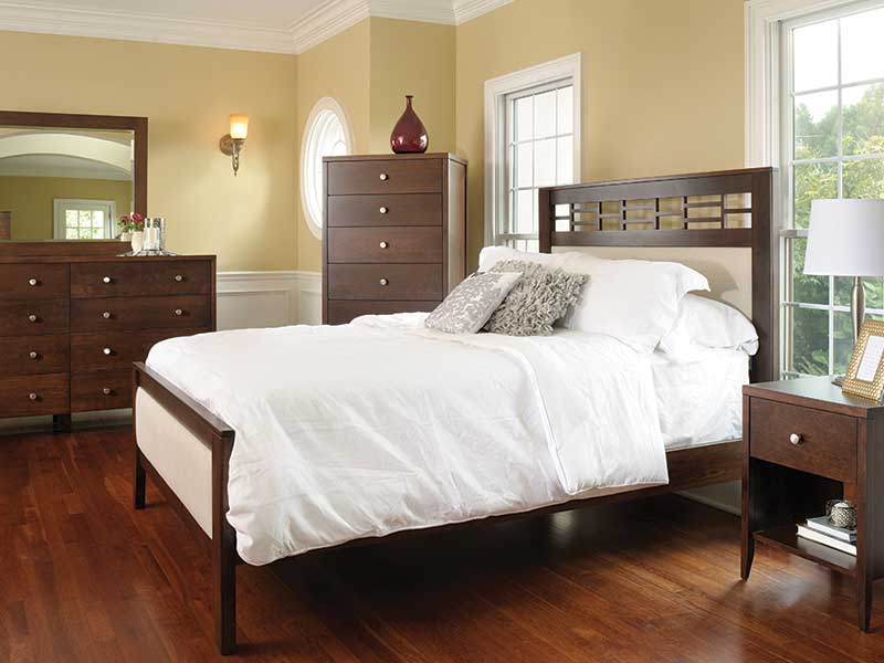 Bedroom scene showing the upholstered Northampton bed dressed in white bedding beside a tall chest, dresser mirror and nightstand