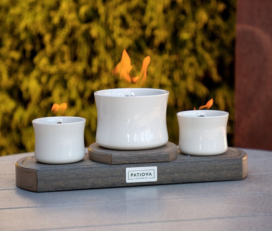 Tabletop fire feature with three white ceramic bowls burning on a gray weathered poly base outdoors at dusk