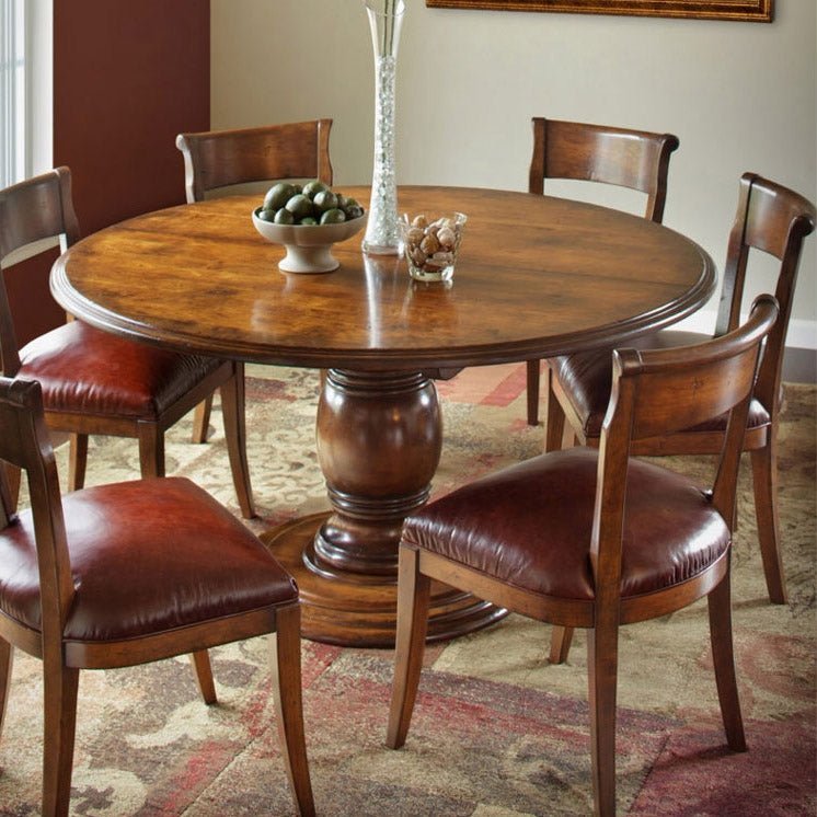 Round rustic cherry dining table with six burgundy leather seat chairs and a glass vase centerpiece