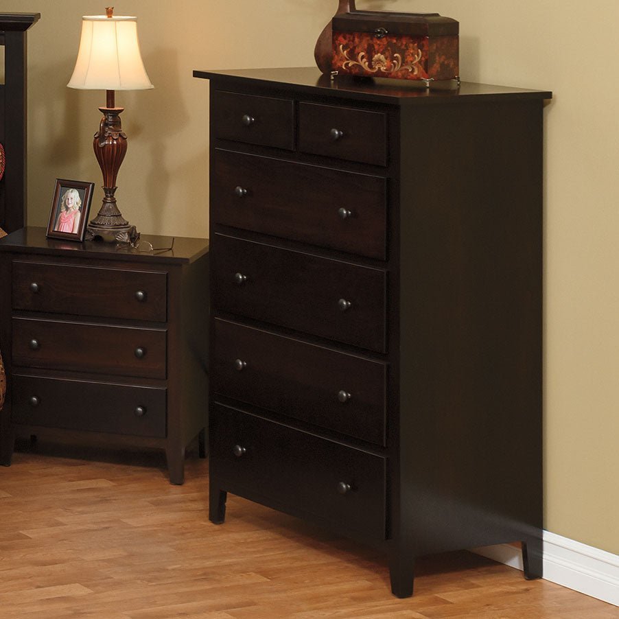 Dark espresso chest of drawers styled in a bedroom with a lamp, framed photo and matching nightstand