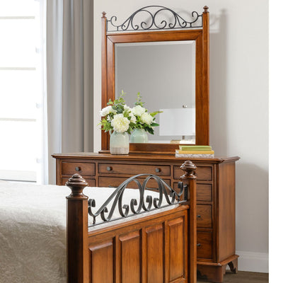 Cherry dresser with an iron scroll topped mirror, white flowers and books beside a scroll bed