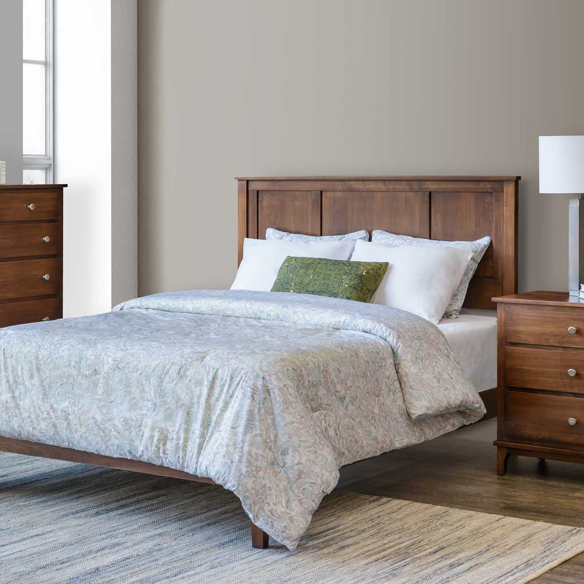 Styled bedroom corner with a Shaker panel bed, matching nightstand and lamp, dressed in soft blue-gray paisley bedding on a woven rug