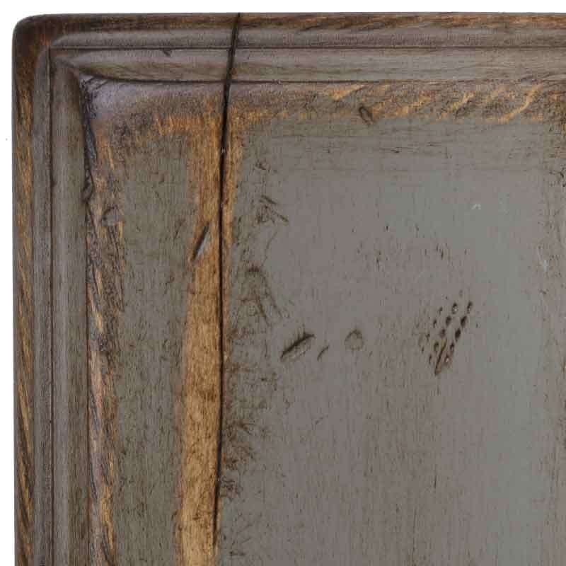 Corner detail of the Chelsea Gray antiqued maple sample, muted gray paint worn along the molding with distress dents and worm holes