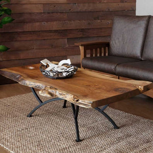 Live edge walnut coffee table on a black arched iron base, styled with a scroll bowl beside a leather sofa