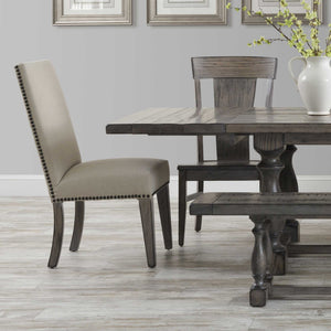 Linen upholstered Corbin dining side chair with dark nailhead trim and gray oak legs beside a weathered trestle table