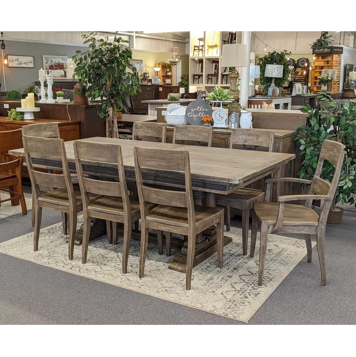 Weathered gray trestle dining table with eight slat back chairs and one arm chair on a patterned rug