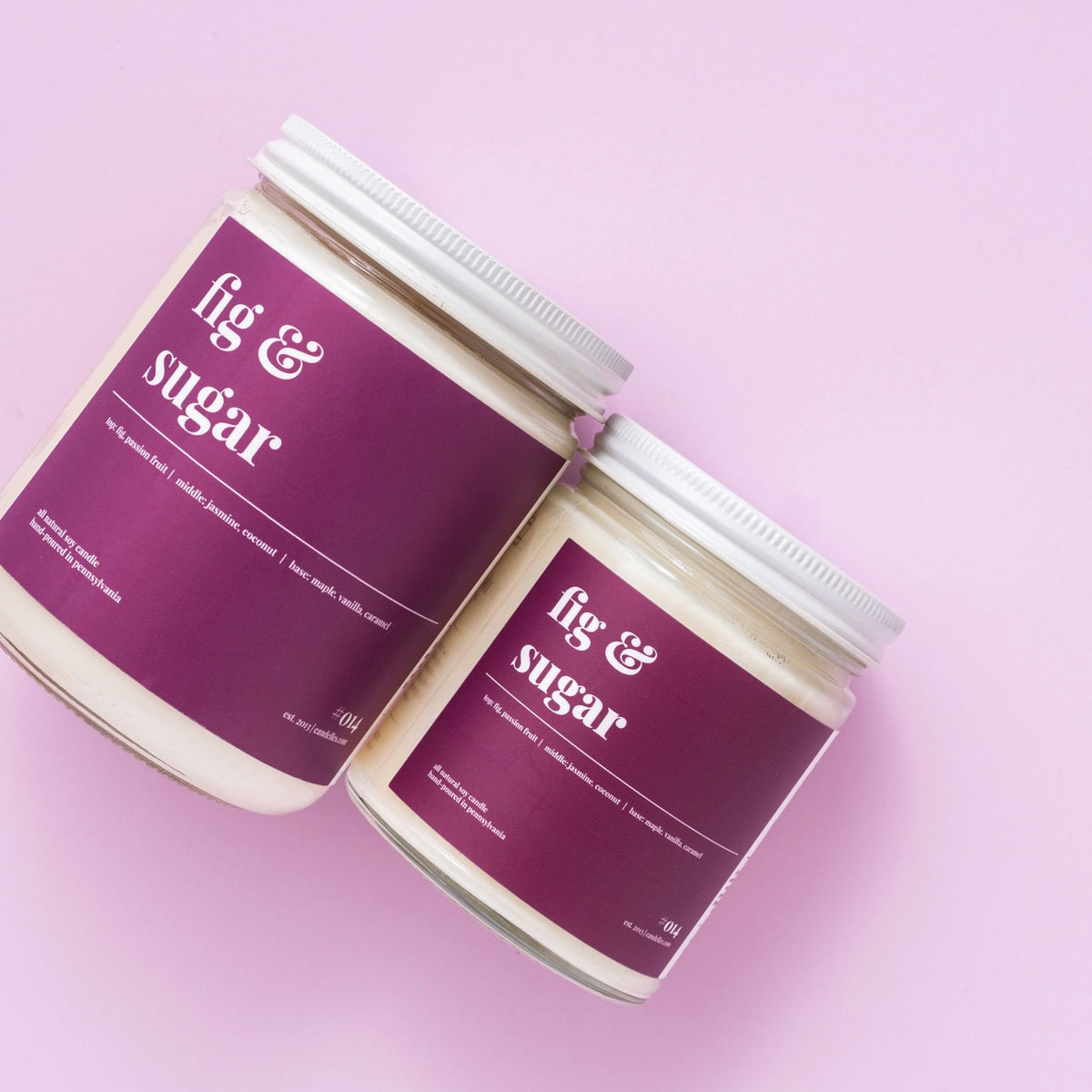 Overhead pair of lidded fig and sugar soy candles in petite and standard sizes on a pale lavender backdrop