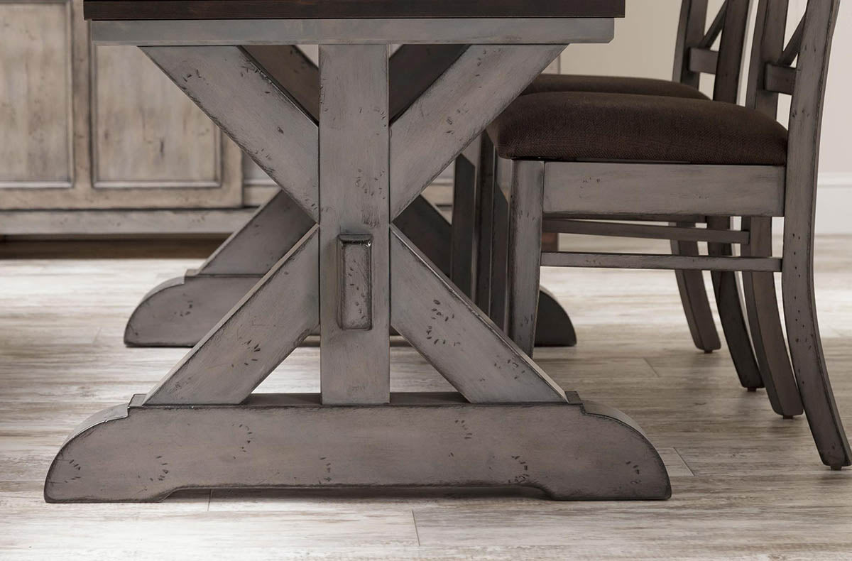 Detail of the trestle table's distressed gray X base with pegged center joint and curved foot