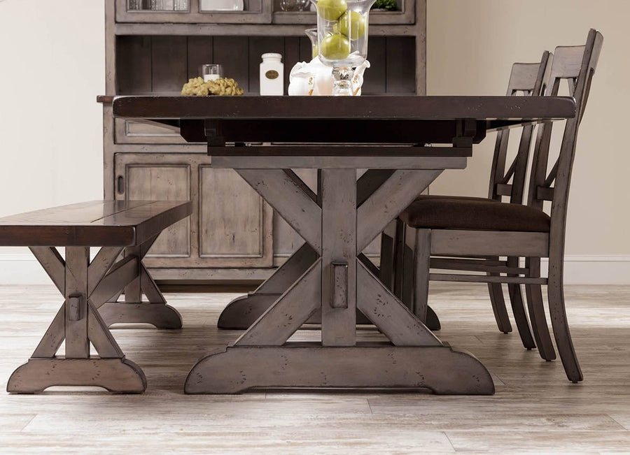 Angled look at the trestle table's dark plank top, gray X base, matching bench and upholstered chairs