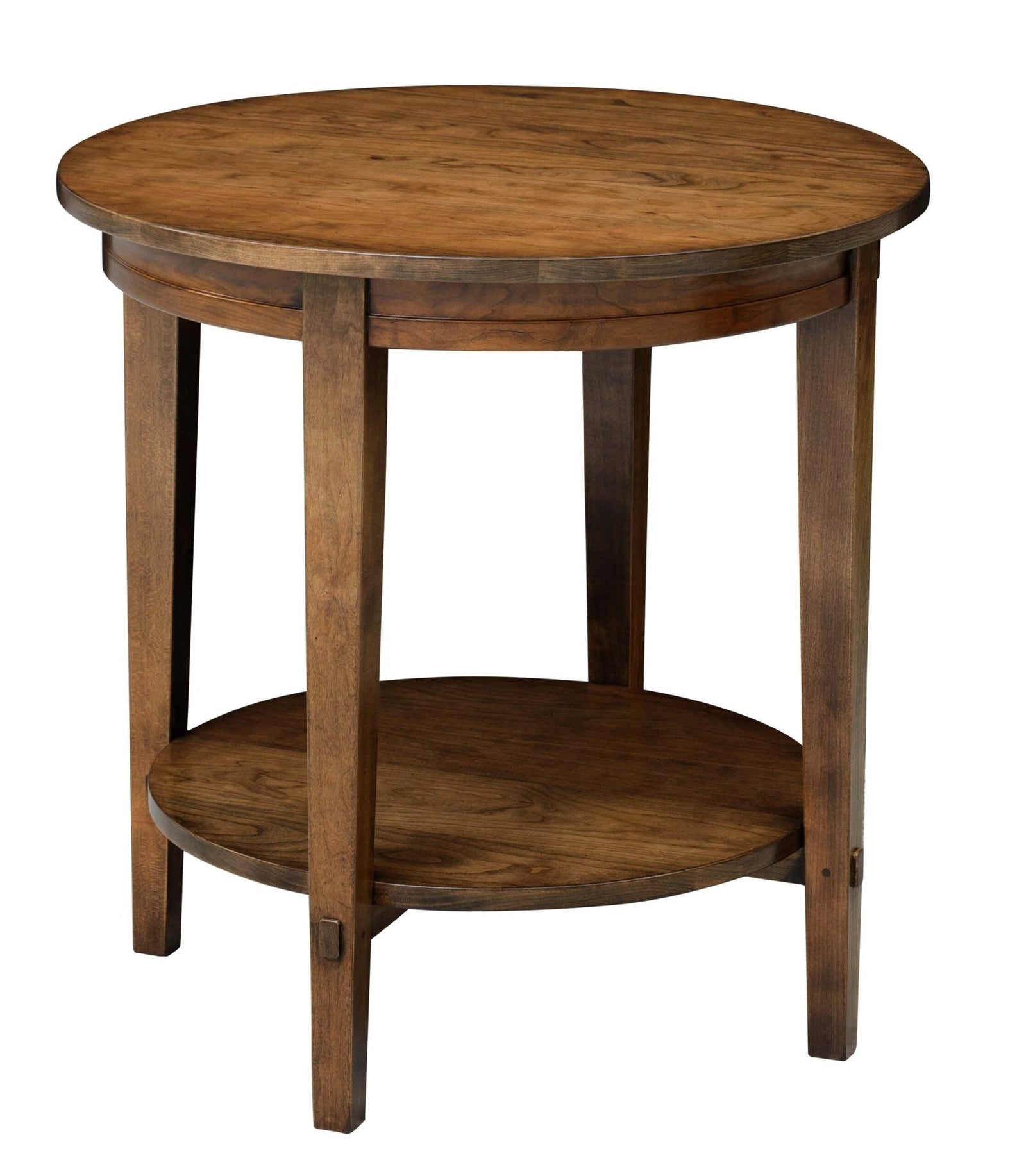 Round wood end table with a lower display shelf holding a fluted lamp beside a brown sofa in a sunlit living room