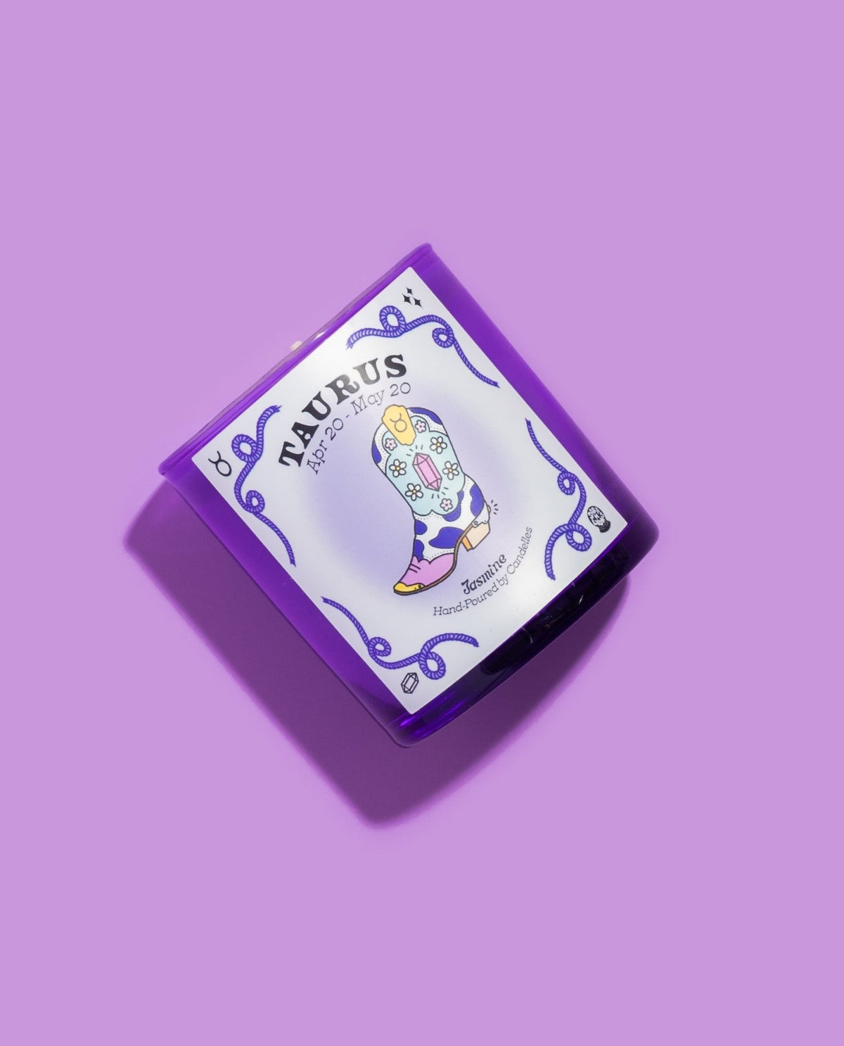 Taurus jasmine zodiac candle angled on a lilac background showing the floral cow print cowboy boot illustration