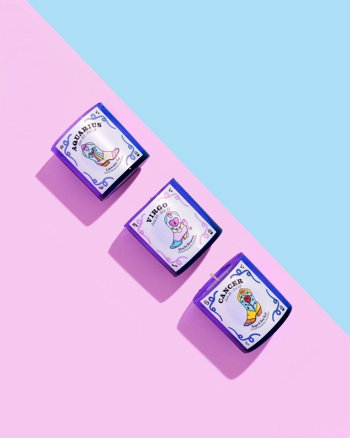 Three purple zodiac candles — Aquarius, Virgo and Cancer — lined diagonally across pink and blue paper