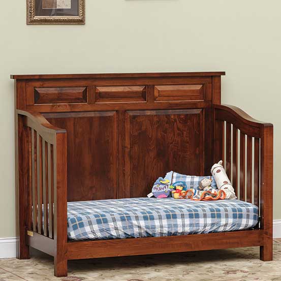 Cherry Princeton crib converted to a day bed with paneled back, open front and blue plaid mattress with toys