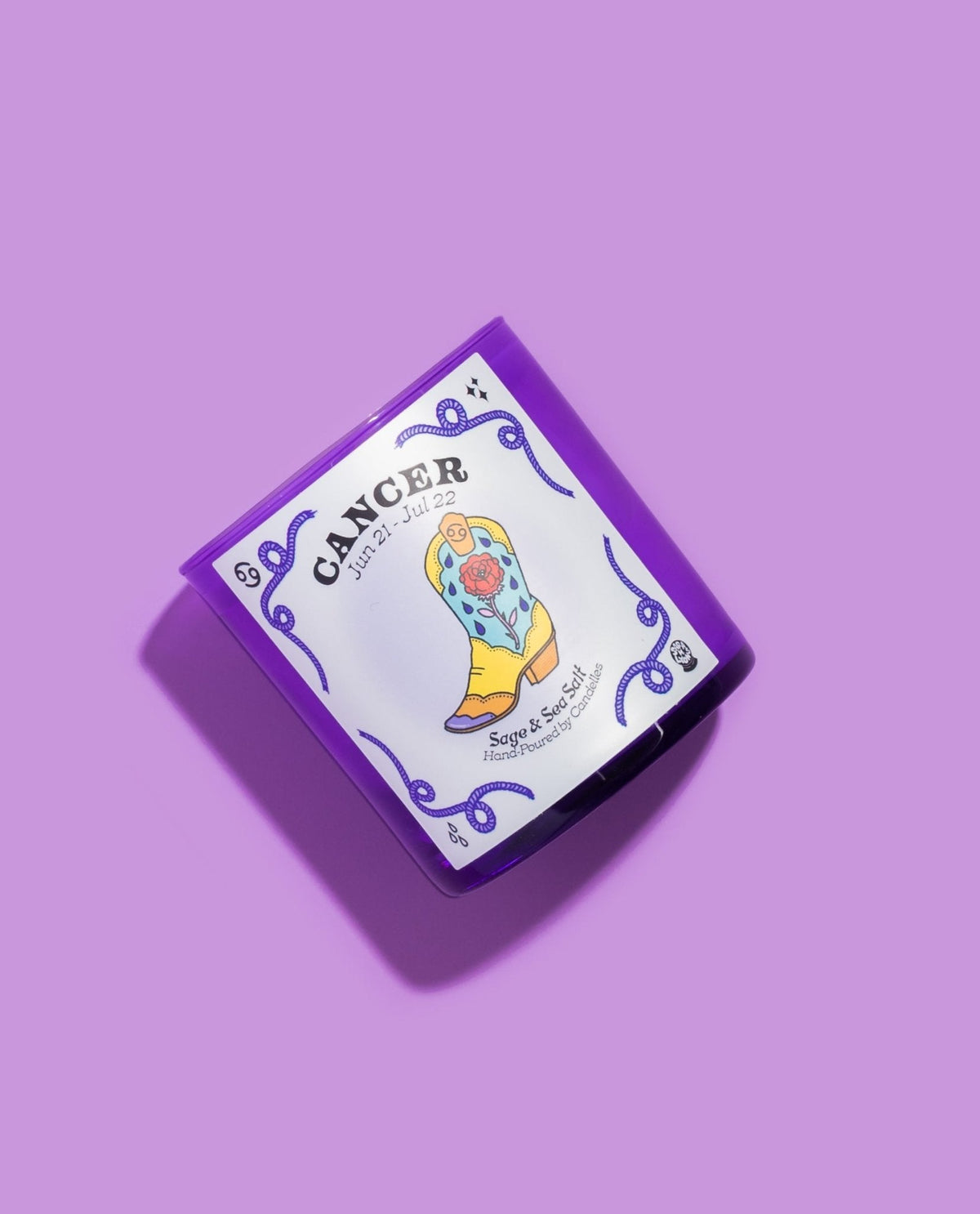 Cancer sage and sea salt zodiac candle tilted on lilac with a yellow rose cowboy boot illustration on the label