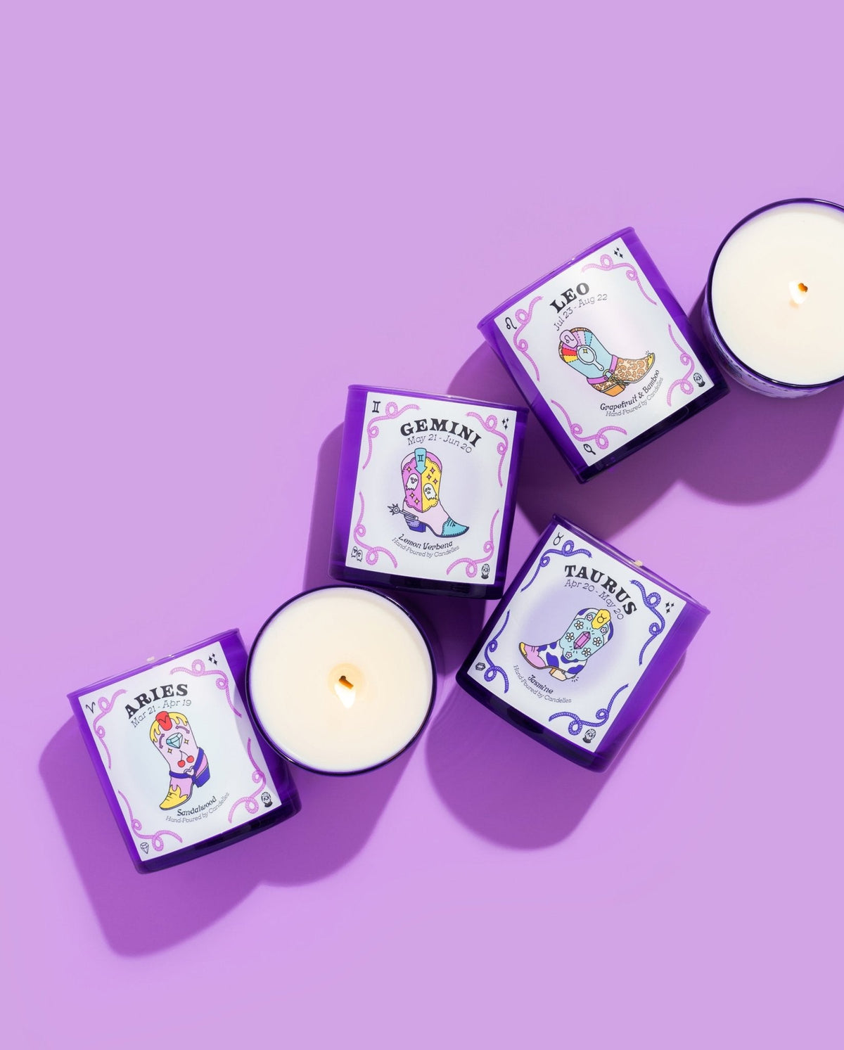 Set of Aries, Gemini, Leo and Taurus purple glass zodiac candles on lilac, two shown lit from above