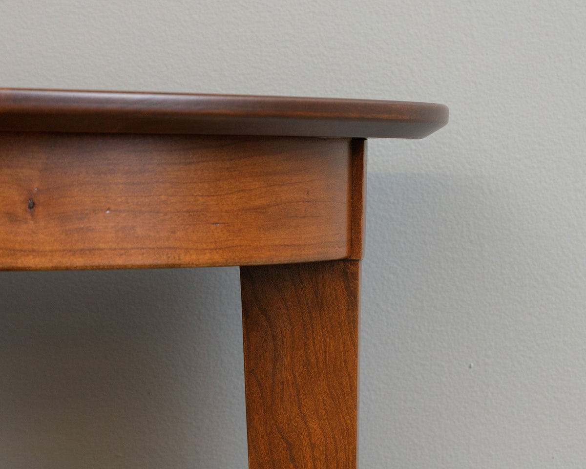 Close up of the coffee table's rounded top edge and apron above a tapered leg in a warm cherry finish