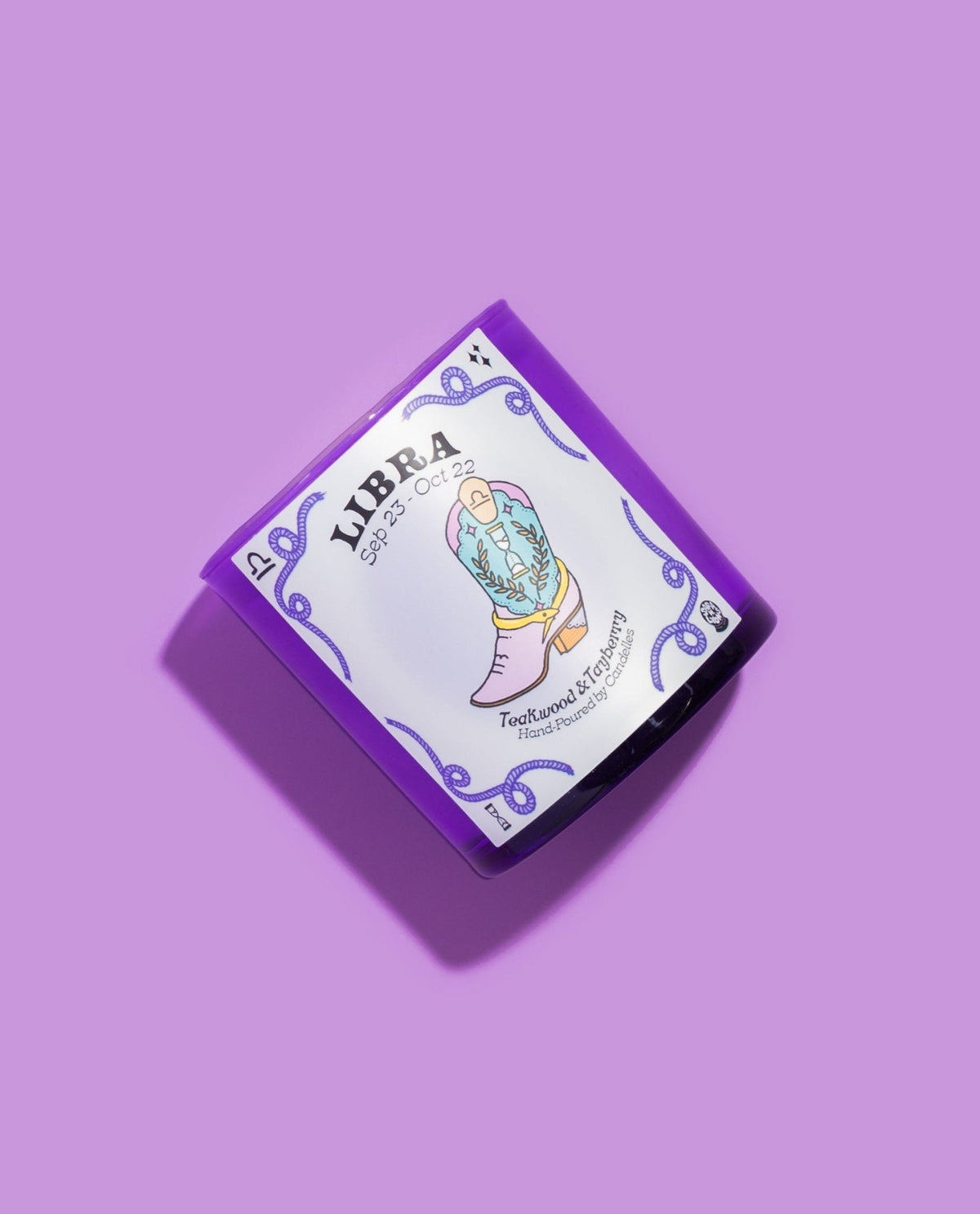 Libra zodiac candle angled on lilac showing the pastel cowboy boot artwork and teakwood and tayberry scent name