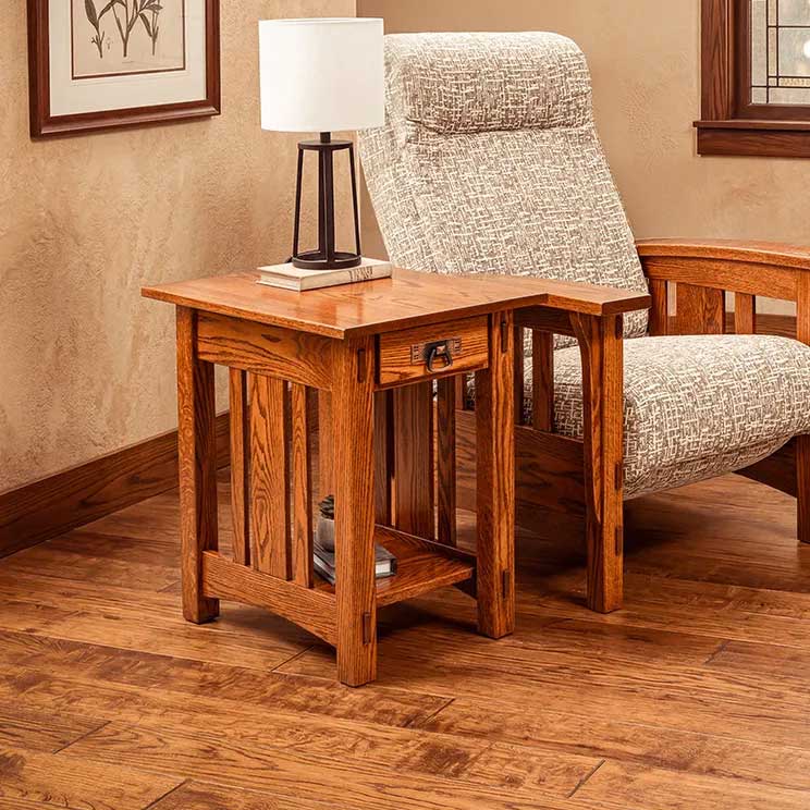 Mission oak end table with a drawer and lower shelf holding books, styled beside a recliner and table lamp